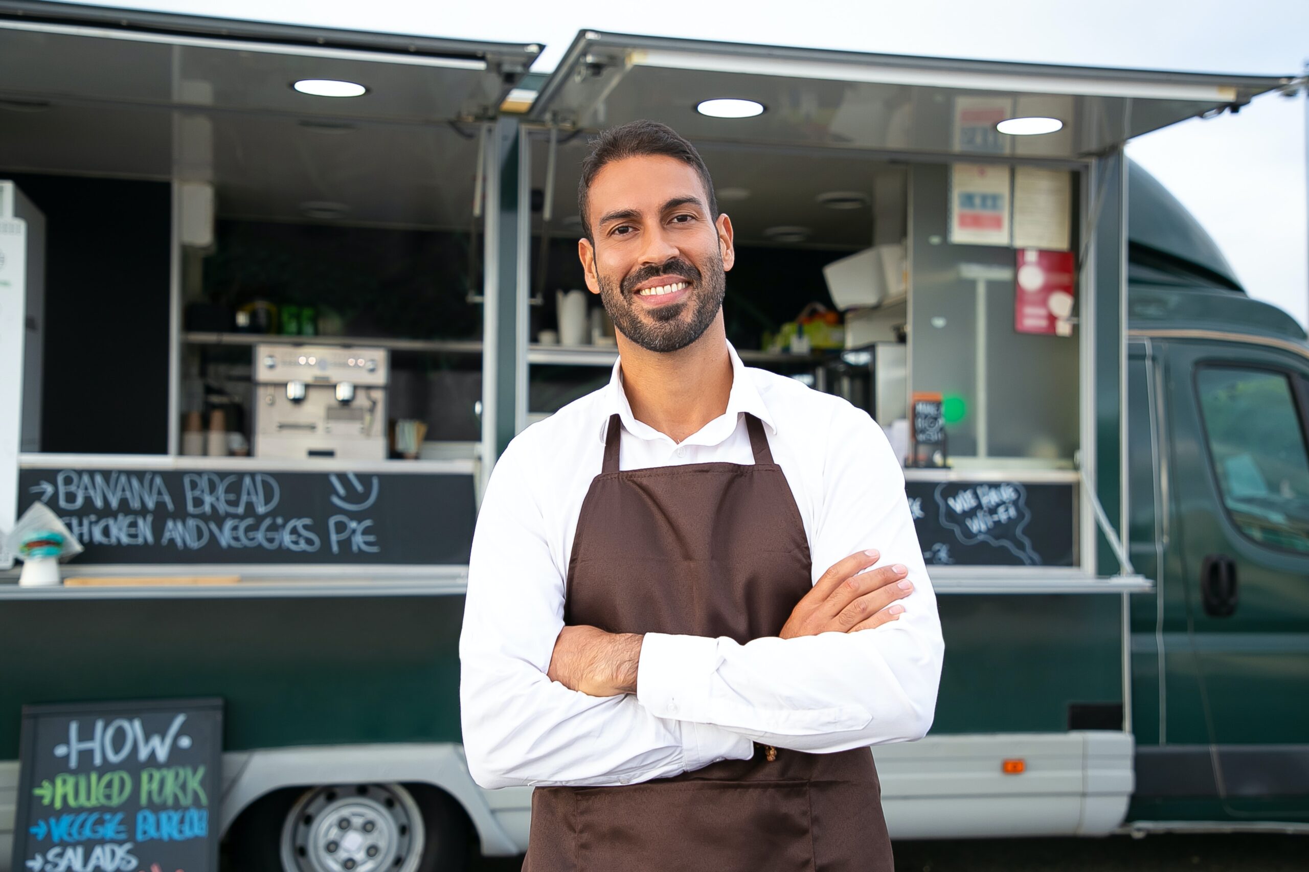 Man standing in front of his food truck in an apron smiling contentedly.